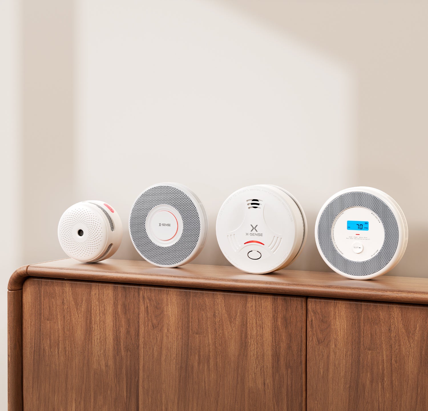 Four smoke detectors on a wooden surface with a neutral background